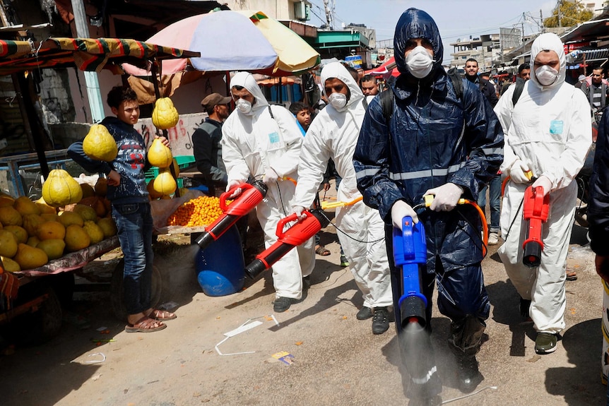 Workers wearing protective gear spray disinfectant as a precaution against the coronavirus in Gaza City.