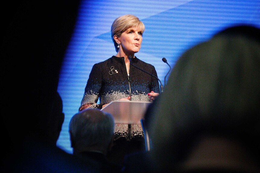 Julie Bishops stands at a podium in front of a blue background.