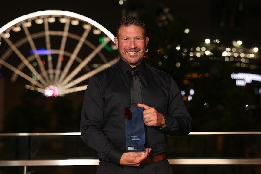 A man in a suit holds a glass award with a ferris wheel lit up in the background.