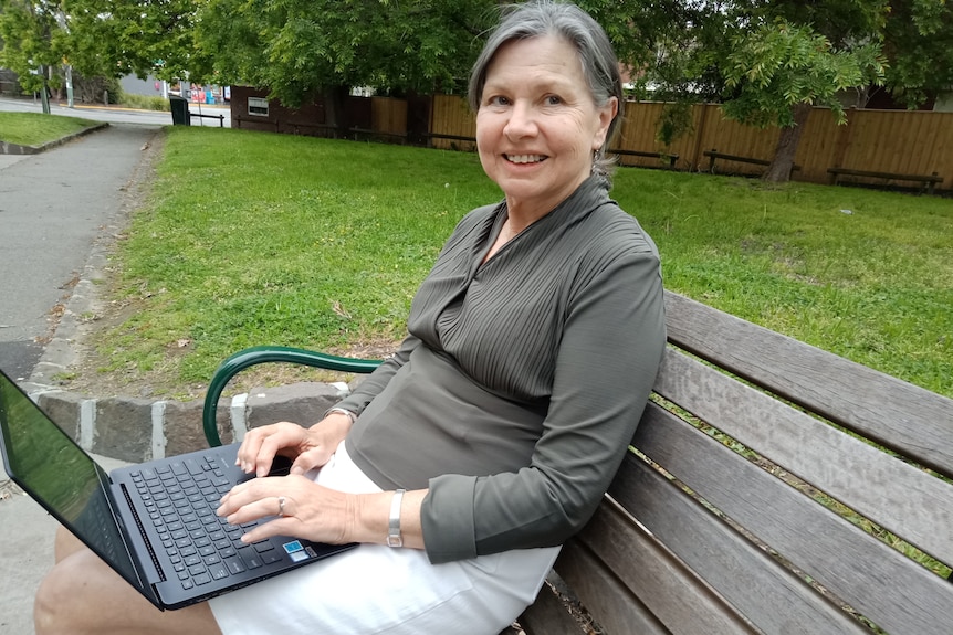 Pam O'Connor sits on a park bench with a laptop.