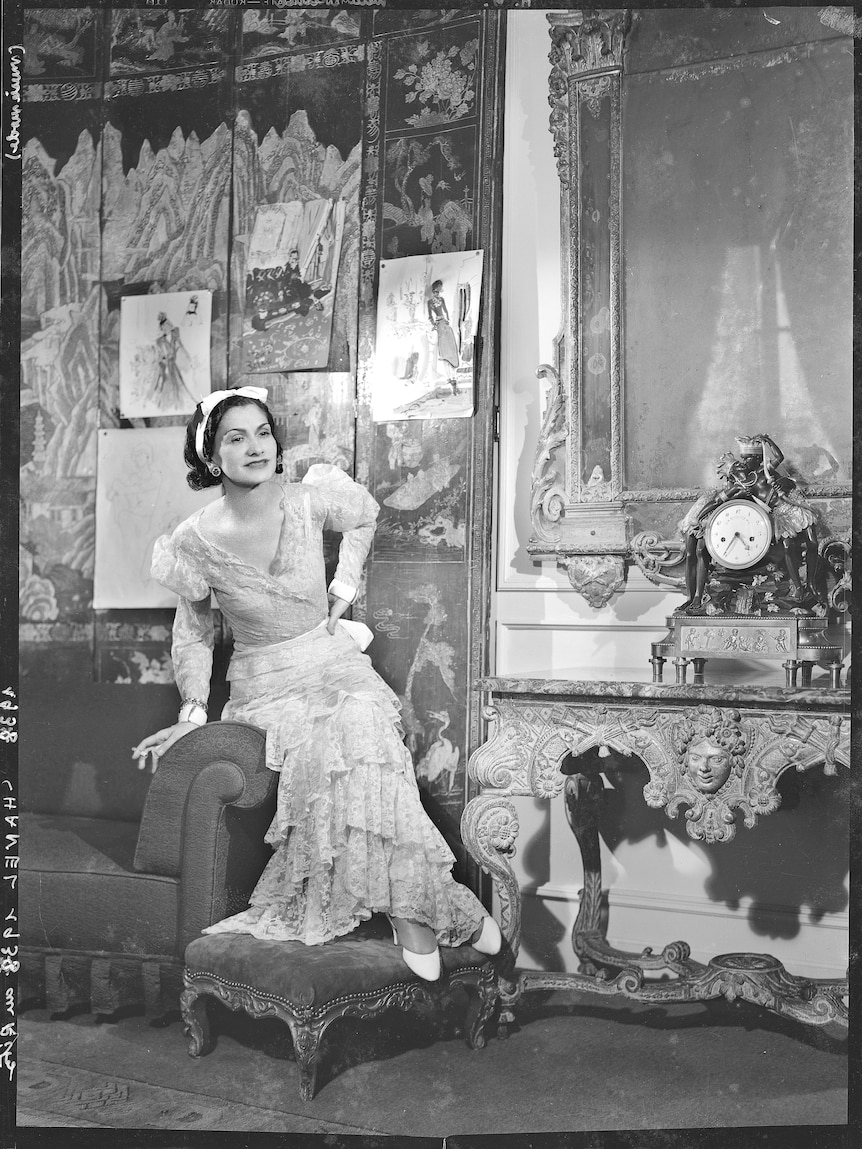 A black and white photo of a woman in the late 1930s in a lacy dress and bow in her hair in a fancy hotel