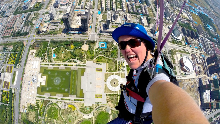 A woman in a helmet skydiving over a city.