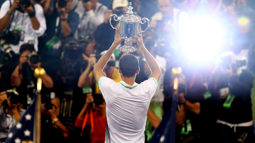 Marin Cilic holds up the US Open trophy to the crowd as cameras flash.