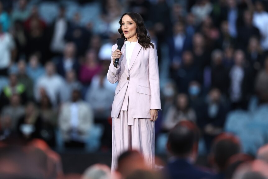 A woman in a pink suit sings in front of a crowd