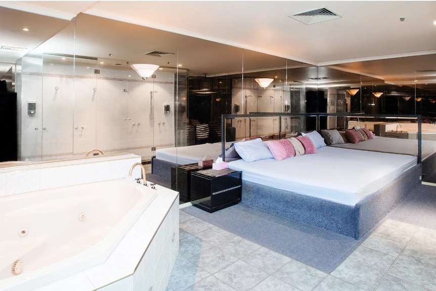 A shot of room with spa, group showers, large bed and mirrors on all walls.