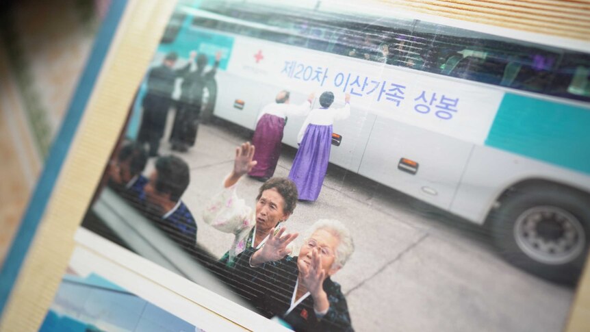 Two women wave tearfully from outside a bus window.