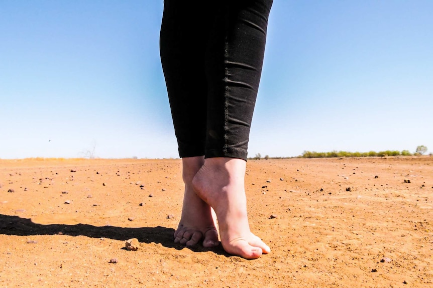 A dancer stands on her toes, ready to begin, in the red dirt at Longreach.