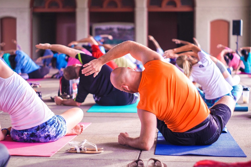 Group of people stretching and sitting on the floor in a yoga class.