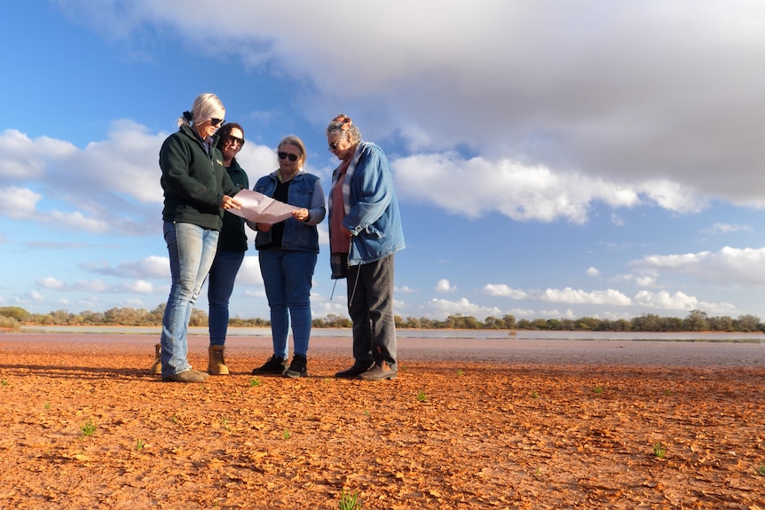 A group of people standing on a dry clay bed looking at a map.
