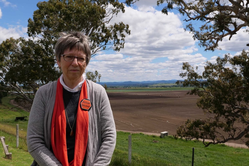 A woman, wearing a badge that says Stop Kalbar, stands in front of a ploughed field