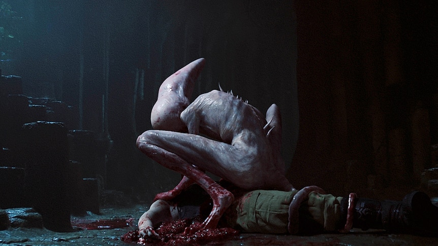 A pale creature with spikes coming out of its back hovers over a bloody body, in the 2017 film Alien Covenant.