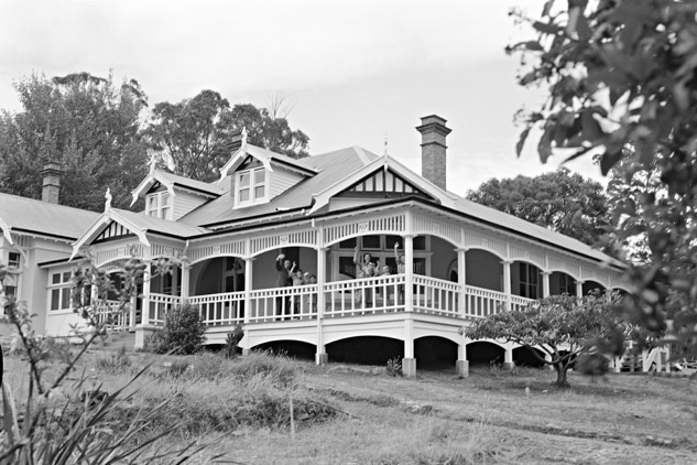 A black and white photo of a large house, raised above the ground on stumps.