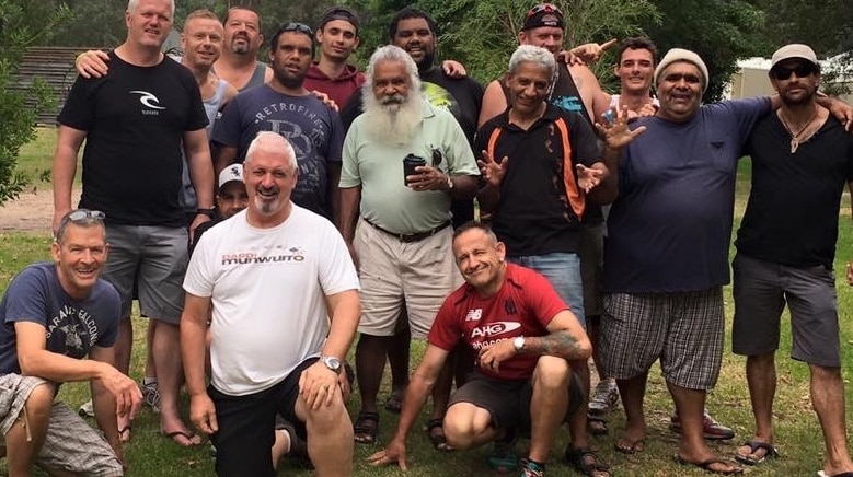 Group of men standing together outdoors all smiling.