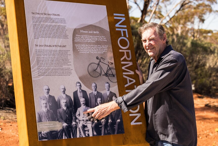 A man pointing to an old photograph at an information board.  