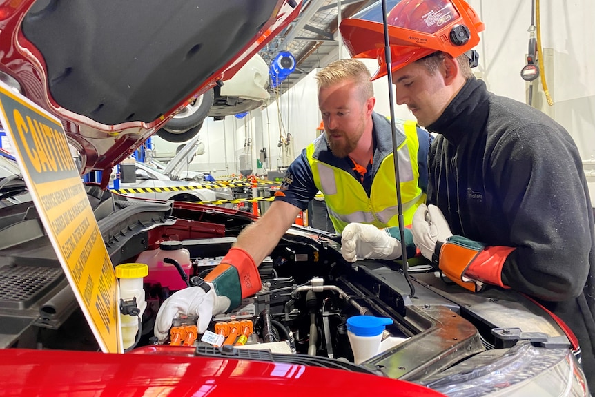 Two men work under the hood of a car.