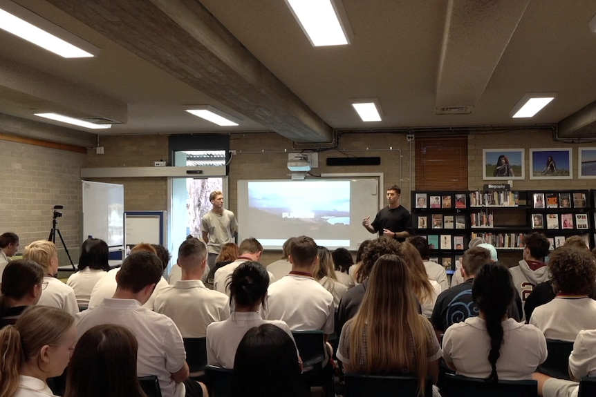 Brett and Bradley address a room of school students sitting down with a project screen between the two of them.