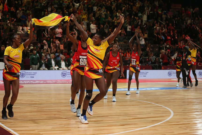 Uganda run out on court holding their national flag as the crowd cheers