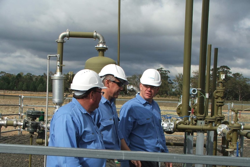 Three men in blue shirts at a gas facility.