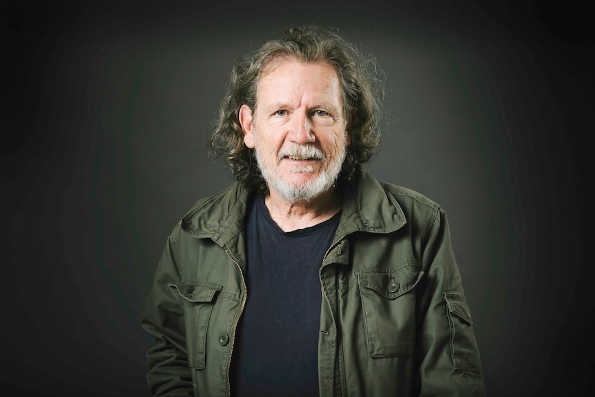 Professor Bryce Barker, wearing a black shirt and khaki jacket, in portrait in front of a dark background