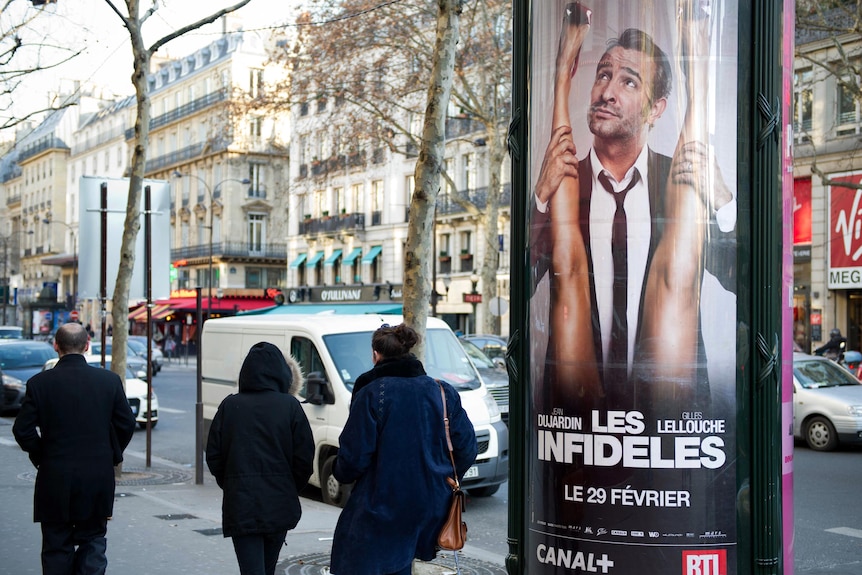 People pass by the film poster of French actor Jean Dujardin for the film Les Infideles in Paris.