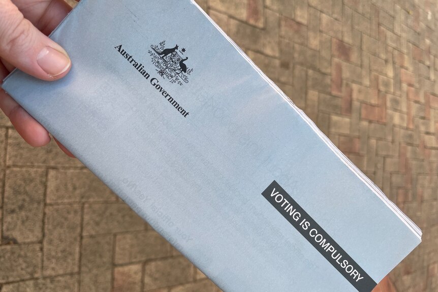 A person holding a Voice to Parliament referendum booklet, which has a federal government logo and says "voting is compulsory" 