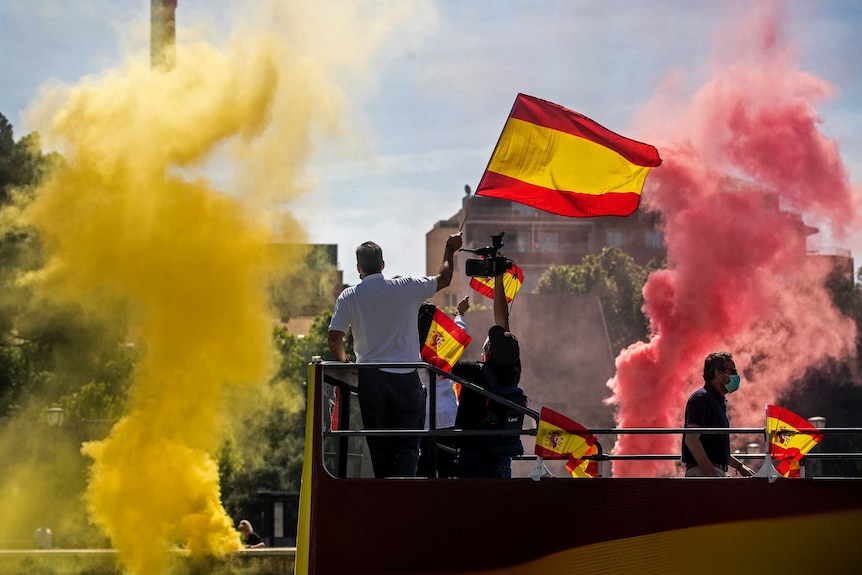 La gente agita banderas españolas mientras queman llamas amarillas y rojas durante una protesta en un autocine organizada por el partido de extrema derecha Vox de España.