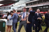Woman leans on man (L), men in suits lift their shirts to show their stomachs (R) in spectator area
