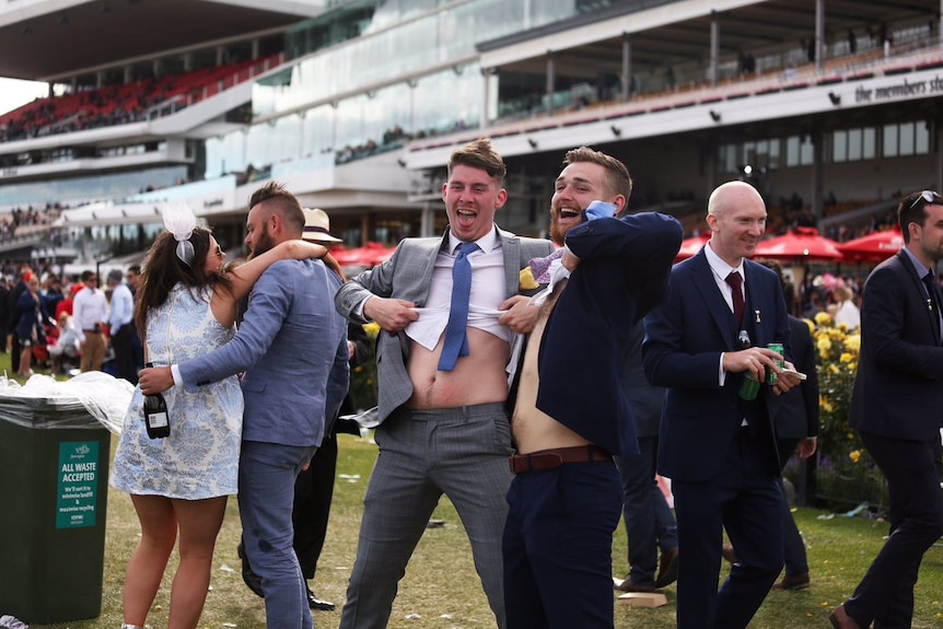 Woman leans on man (L), men in suits lift their shirts to show their stomachs (R) in spectator area