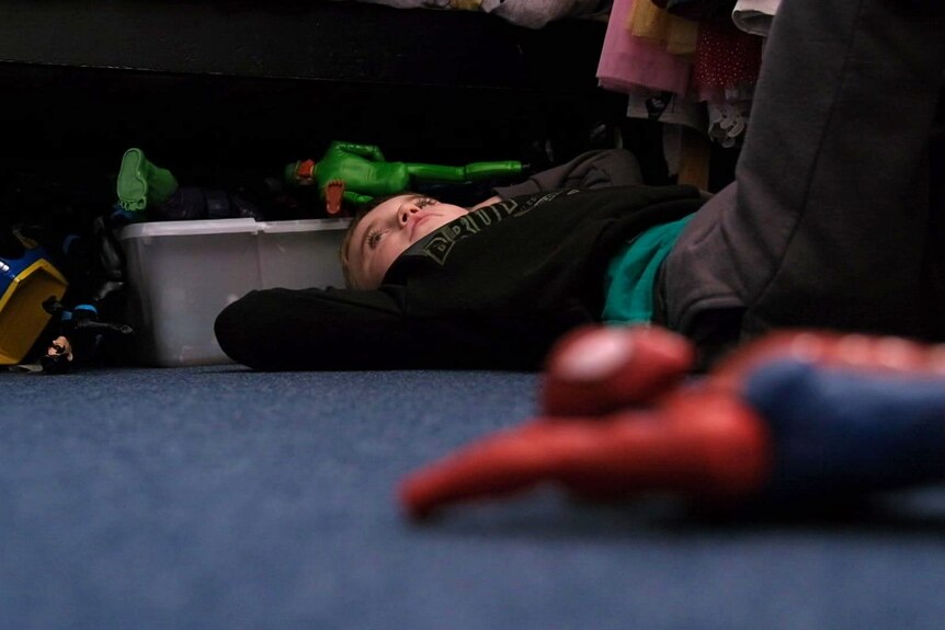 A young boy lies on the floor next to a Spiderman toy