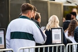 A man standing in line scanning a Safe WA QR code.