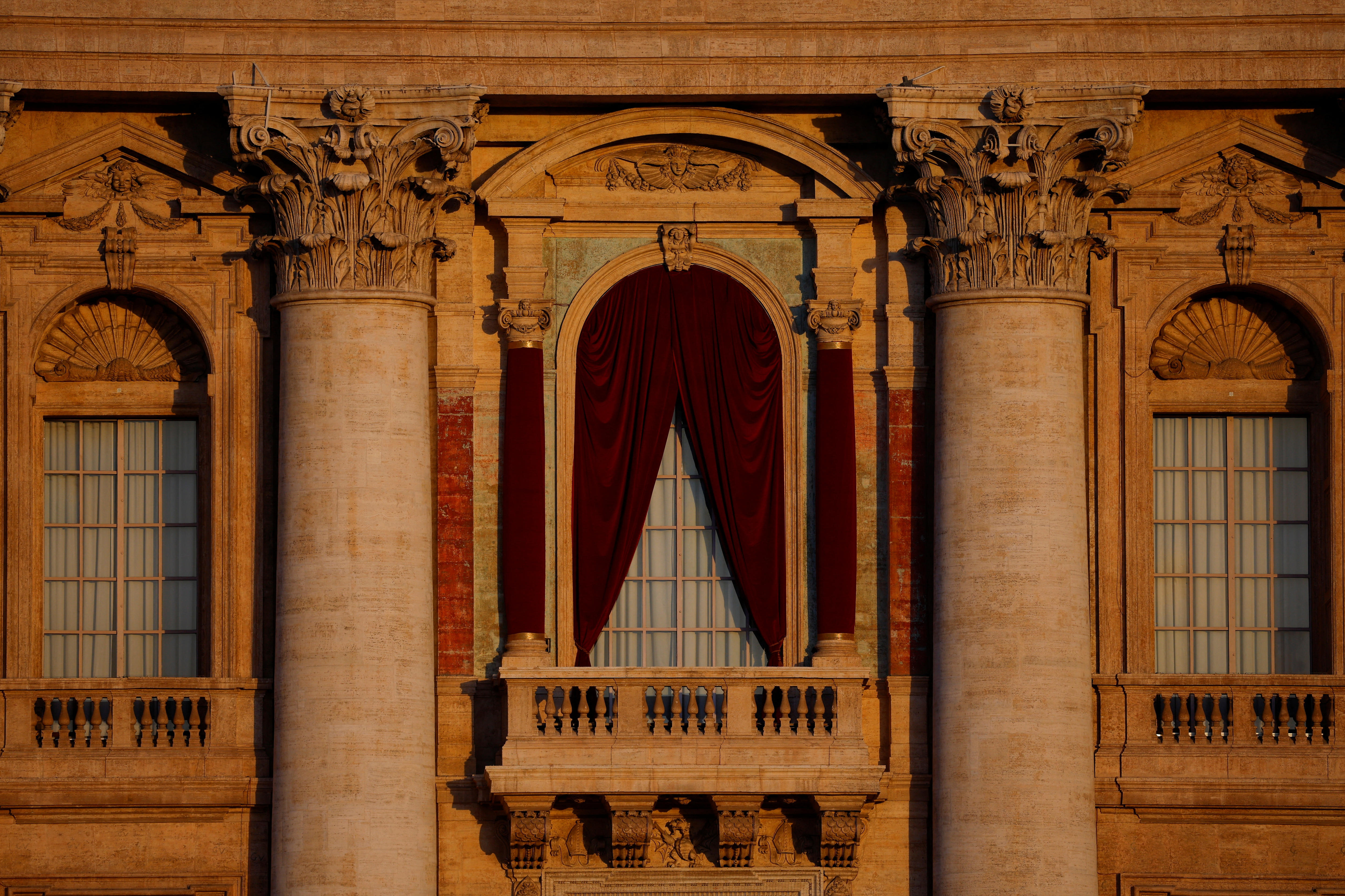 A fachada de um antigo edifício de pedra ornamentado, mostrando uma janela de varanda com cortinas meio fechadas entre dois pilares.