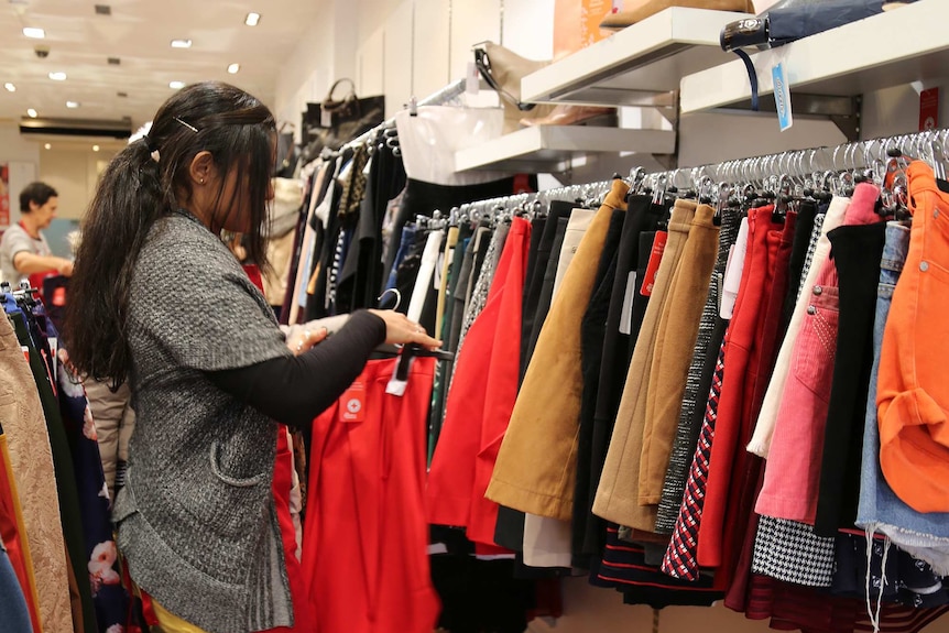 A lady wearing a grey cardigan and a red 'Red Cross' apron puts a red skirt back on a hanger.