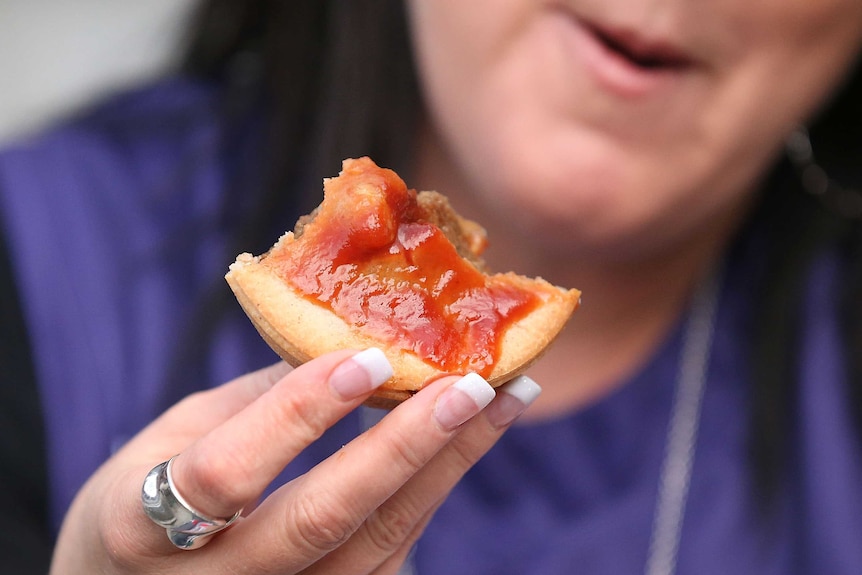 A woman eats a meat pie covered in sauce with her hands.