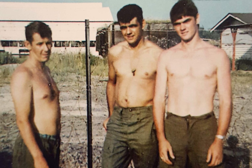 Three soldiers stand shirtless in Vietnam.