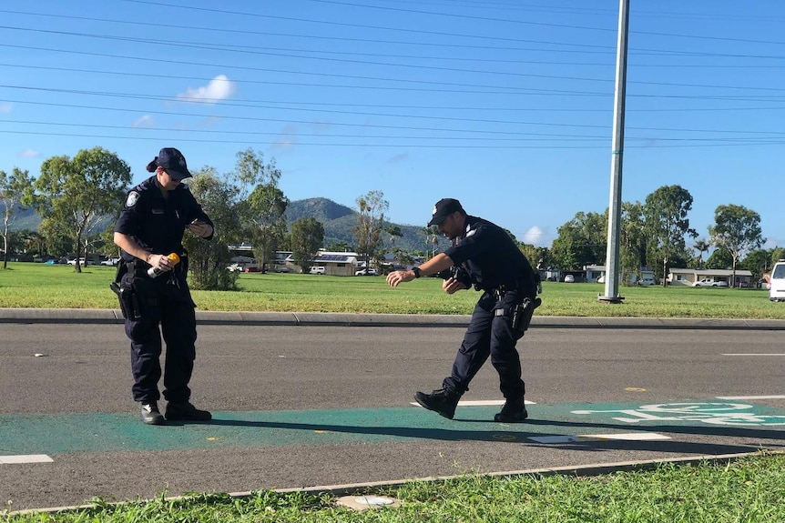 Two police officers use spray paint to mark evidence of cyclists' hit-and-run.