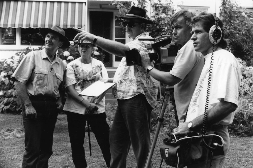 Black and white photo of ABC camera crew filming with Peter Cundall watching on in garden.