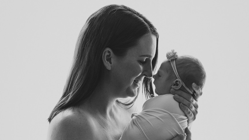 A black and white portrait of Lauren holding her baby daughter Daisy close to her face and smiling.