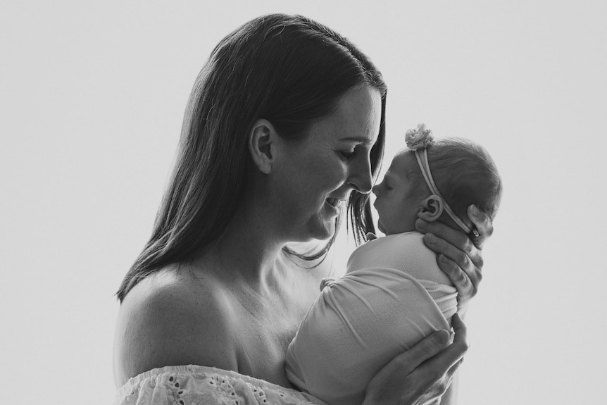 A black and white portrait of Lauren holding her baby daughter Daisy close to her face and smiling.