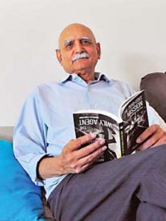 An older man with white moustache and eyebrows reclines on a couch with a book on his lap