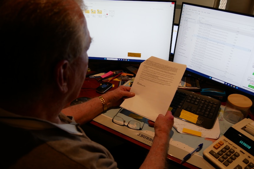 A man with greying hair reads over a white page, black letter letter