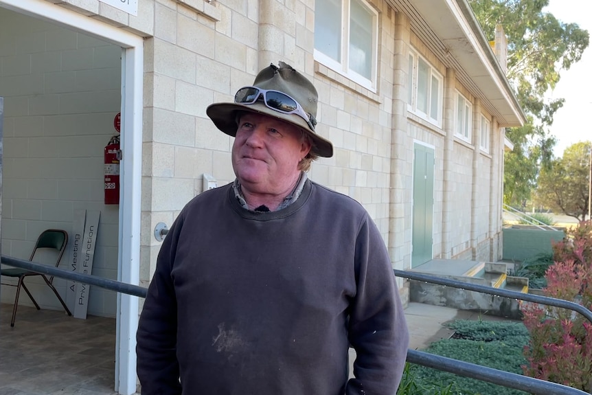 A man in a jumper and hat stands in front of a building.