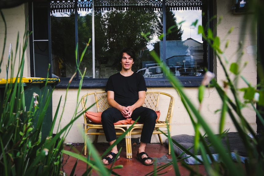 Henry sits on a wicker couch on the front porch of a house