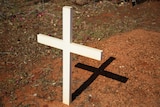 A simple wooden cross in the ground at an outback cemetery.