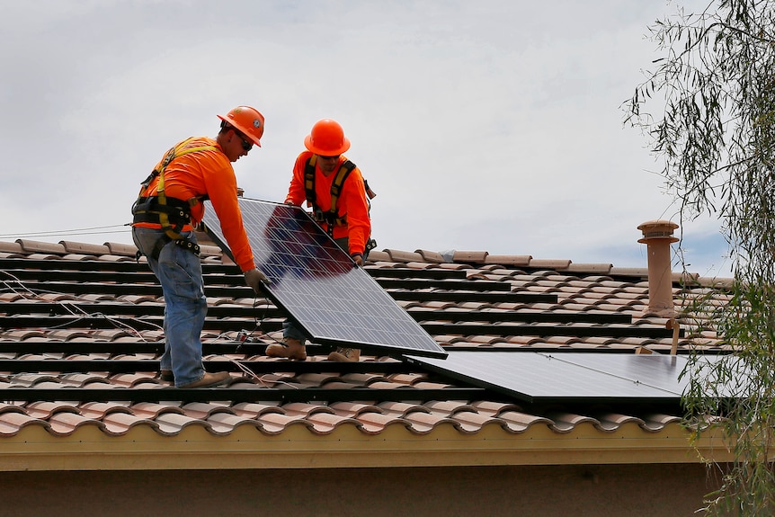 Two men in orange workwear install a solar panel