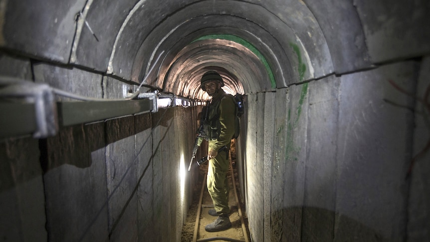 An Israeli army officer stands inside a narrow underground tunnel holding a firearm.