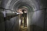 An Israeli army officer stands inside a narrow underground tunnel holding a firearm.