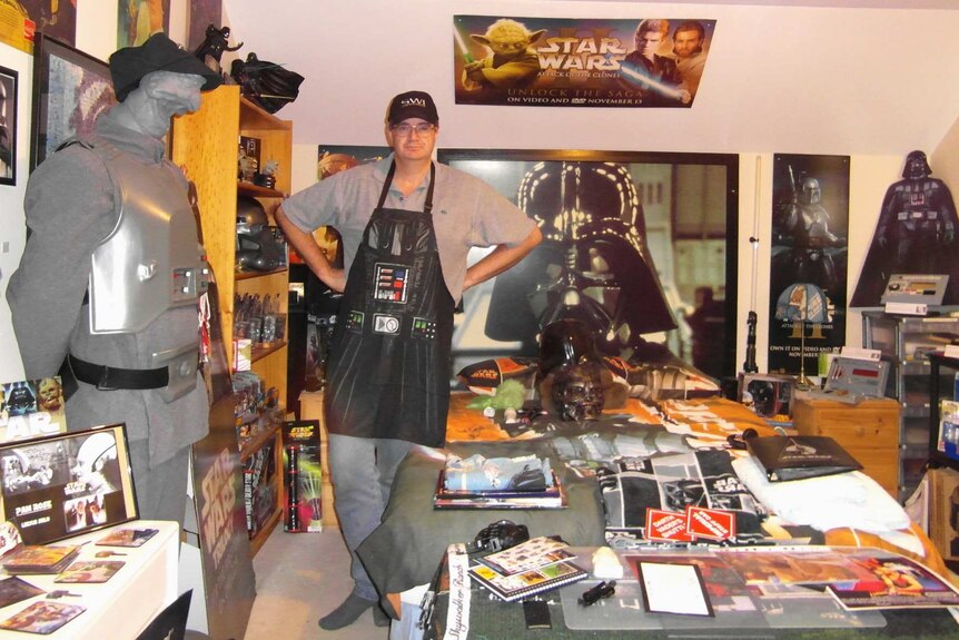 A man stands in a room filled with Star Wars paraphernalia