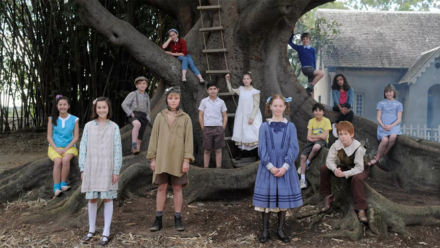 Young children in period dress from different historical eras gathered around a large tree