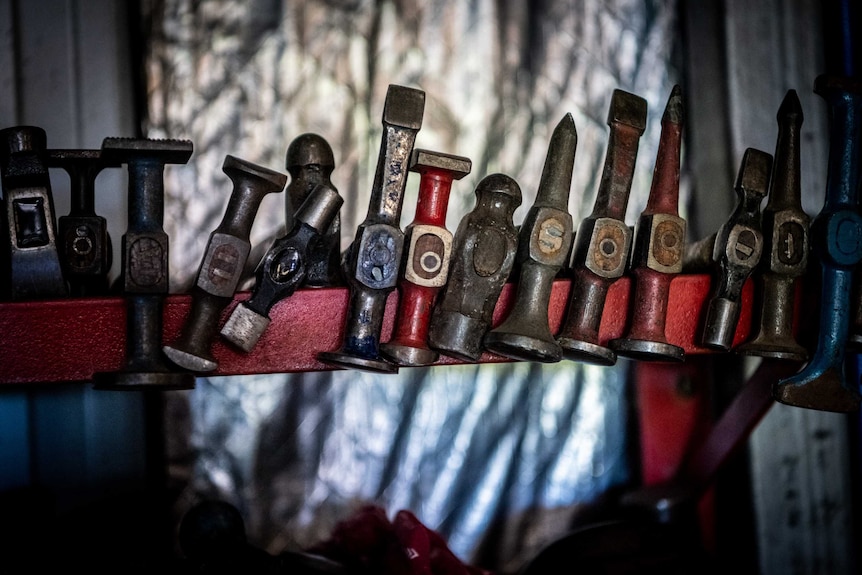 A row of hammers rest on a red metal beam.