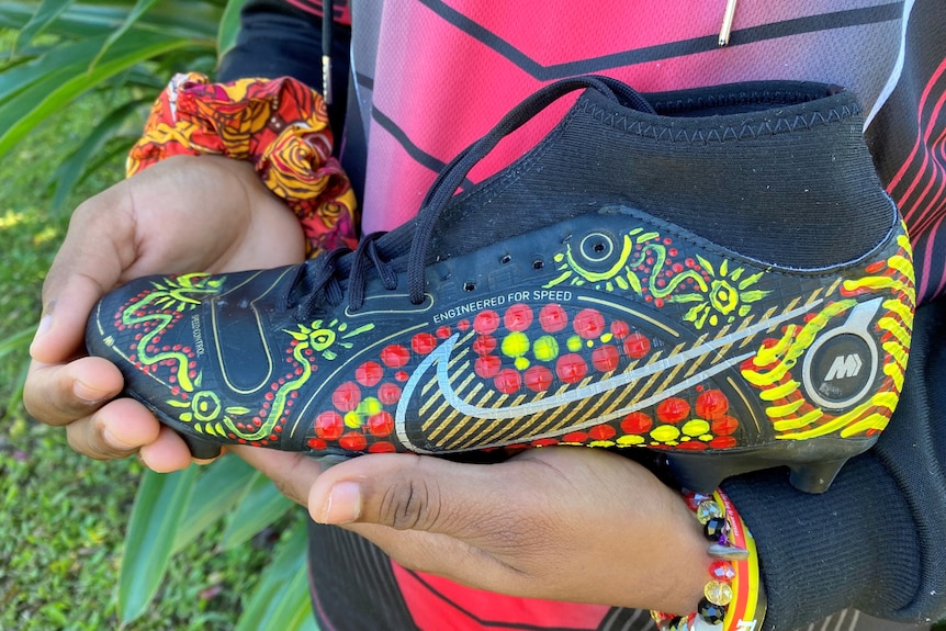 Young woman holds a football boot with Aboriginal painting on it